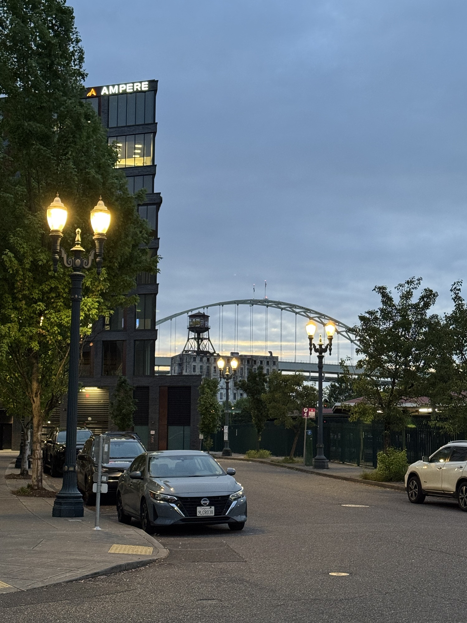 An evening Portland street with lamps, trees, and a bridge in the background